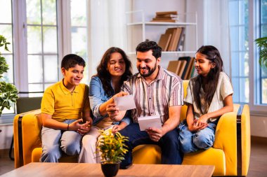 Hintli genç bir aile, evde eski fotoğrafları seyrederken birlikte mutlu anıları hatırlarken modern bir oturma odasındaki kanepede oturup gülüşmeler, duygusal aile anlarının tadını çıkarıyordu.