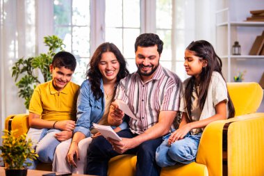 Hintli genç bir aile, evde eski fotoğrafları seyrederken birlikte mutlu anıları hatırlarken modern bir oturma odasındaki kanepede oturup gülüşmeler, duygusal aile anlarının tadını çıkarıyordu.