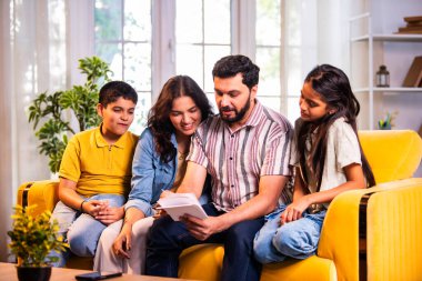 Hintli genç bir aile, evde eski fotoğrafları seyrederken birlikte mutlu anıları hatırlarken modern bir oturma odasındaki kanepede oturup gülüşmeler, duygusal aile anlarının tadını çıkarıyordu.