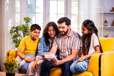 Hintli genç bir aile, evde eski fotoğrafları seyrederken birlikte mutlu anıları hatırlarken modern bir oturma odasındaki kanepede oturup gülüşmeler, duygusal aile anlarının tadını çıkarıyordu.