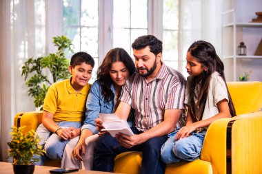 Hintli genç bir aile, evde eski fotoğrafları seyrederken birlikte mutlu anıları hatırlarken modern bir oturma odasındaki kanepede oturup gülüşmeler, duygusal aile anlarının tadını çıkarıyordu.