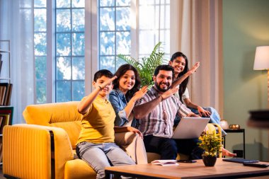 Hintli genç bir aile evlerinde dizüstü bilgisayar kullanıyor. Kanepede birlikte oturuyor. İnternette sörf yapıyor ve içeriden alışveriş yapıyor.