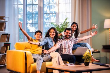 Hintli genç bir aile evlerinde dizüstü bilgisayar kullanıyor. Kanepede birlikte oturuyor. İnternette sörf yapıyor ve içeriden alışveriş yapıyor.