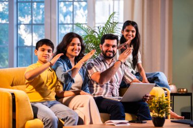 Hintli genç bir aile evlerinde dizüstü bilgisayar kullanıyor. Kanepede birlikte oturuyor. İnternette sörf yapıyor ve içeriden alışveriş yapıyor.