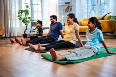 Hintli aile yog asana yapıyor. Yoga seansları arasında bacaklarını dinlendiriyorlar. Sabahları sakin bir şekilde evde oturuyorlar.