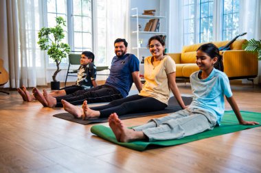 Hintli aile yog asana yapıyor. Yoga seansları arasında bacaklarını dinlendiriyorlar. Sabahları sakin bir şekilde evde oturuyorlar.