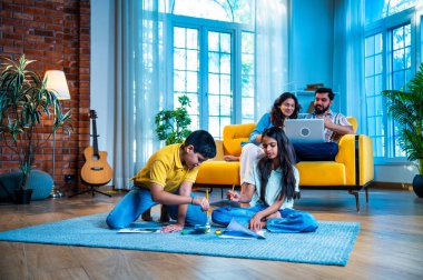 Hintli çocuklar sanatla meşgulken, ebeveynler evde kanepede oturur kardeşler halıya resim çizerken ve genç anne baba modern oturma odasında dizüstü bilgisayar ve akıllı telefon kullanarak sohbet ederken.