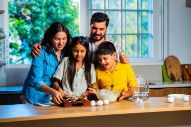 Hint ailesi, modern mutfakta kek hamuru yaparken genç ebeveynler, hamuru karıştırırken kaliteli zaman geçirmenin, bağ kurmanın ve neşeli ev yemeği pişirmenin keyfini çıkarıyorlar.