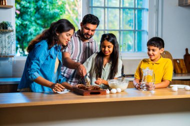 Hint ailesi, modern mutfakta kek hamuru yaparken genç ebeveynler, hamuru karıştırırken kaliteli zaman geçirmenin, bağ kurmanın ve neşeli ev yemeği pişirmenin keyfini çıkarıyorlar.