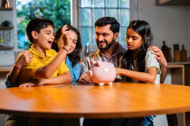 Modern evdeki domuz kumbarasında dört madeni paradan oluşan Hintli genç aile, erkek ve kız çocuklarına para disiplini, finansal planlama, gelecekteki güvenlik ve iyi tasarruf alışkanlıklarının önemini öğretiyor.