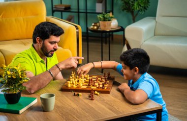 Hintli genç baba oğul evde satranç oynuyor arkadaşça rekabet ve spor rekabetinin tadını çıkarıyor, birlikte strateji öğrenirken modern oturma odasında kaliteli aile zamanı geçiriyor.