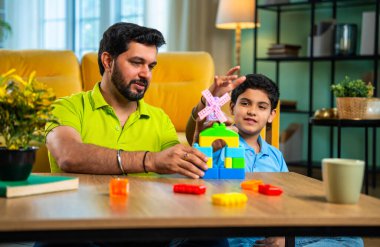 Hintli genç baba oğul, neşeli atmosferde oyuncak yel değirmeni inşa ediyor renkli plastik kule yaratıyor ve modern oturma odasında kaliteli bir aile zamanı geçiriyor.