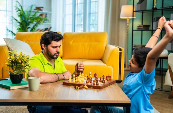 Hintli genç baba oğul evde satranç oynuyor arkadaşça rekabet ve spor rekabetinin tadını çıkarıyor, birlikte strateji öğrenirken modern oturma odasında kaliteli aile zamanı geçiriyor.