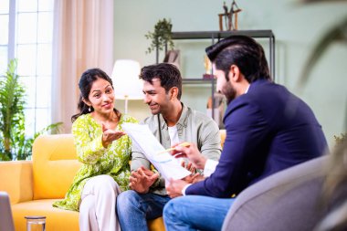 Hintli çift yatırım toplantısı sırasında temsilciyle tartışıyor. İş adamlarıyla mali belgeleri ve dosyaları gözden geçiriyorlar. Bu sırada rahat, modern oturma odasındaki koltukta oturuyorlar.