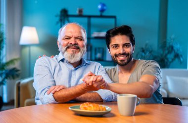 Hintli genç oğlu, modern oturma odasındaki babasıyla neşeyle konuşuyor. İki kuşak arasında iç açıcı bir aile sohbeti. Tavsiyelerini, bilgeliğini, mutluluğunu ve gülümsemesini paylaşıyor.