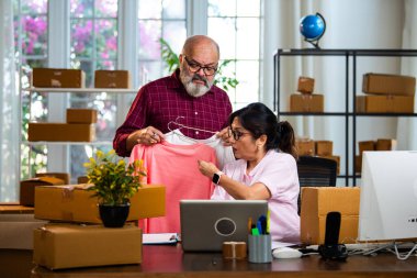 Hintli üst düzey çift bilgisayar sistemine ürün detaylarını giriyor ev idaresinden internet siparişlerini yapıyor, paketlerle uğraşıyor, tişört kataloğunu güncelliyor ve mutlu bir şekilde çalışıyor.