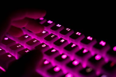 perspektif kenar görünümü detayı, aydınlatmalı mekanik oyun RGB klavyesinde yazan erkek parmaklarının koyu kırmızı tuş kapakları ile yakın çekim görüntüsü