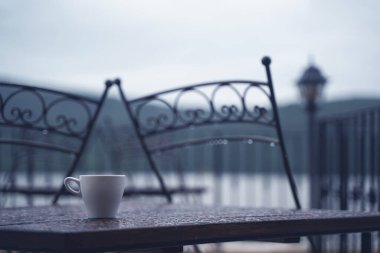Beyaz espresso fincanının yakın plan detayları ahşap masanın üzerinde yağmurlu açık hava restoranlarının terasında yağmur damlaları var. 