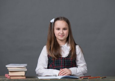 Tek tip bir okulda kız kitapları, gri arka plan ile bir masada oturan bir tebeşir tahtası gibi görünüyor