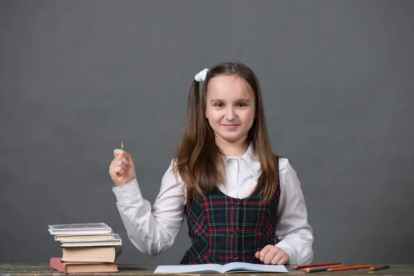 Dziewczyna w szkole jednolitego siedzi przy stole z książek, szare tło, wygląda jak chalk zarządu — Zdjęcie stockowe
