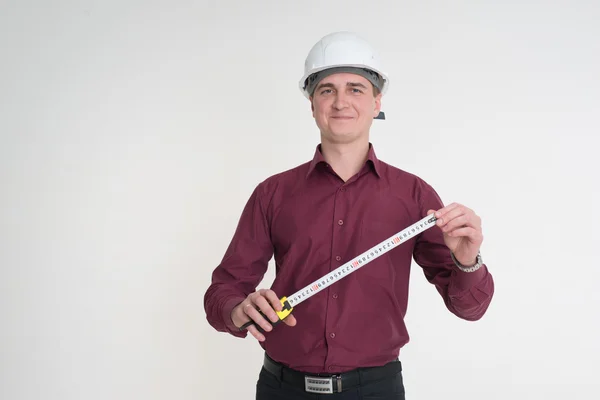 Un hombre con una camisa marrón y en el casco de construcción con una cinta métrica para medir la distancia —  Fotos de Stock