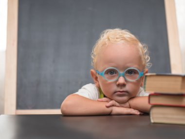 Gözlüklü çocuk kitapları ile bir masada oturur 