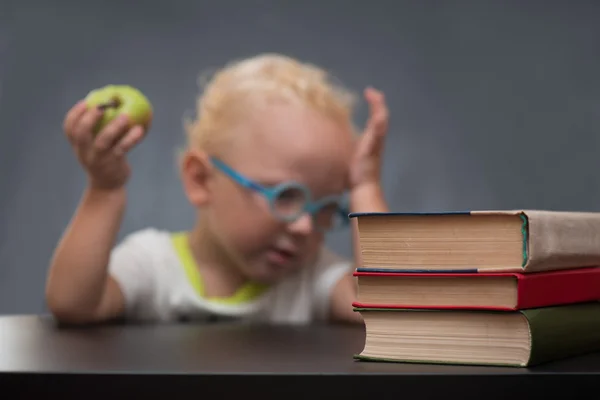 Criança com copos senta-se em uma mesa com livros e maçã — Fotografia de Stock