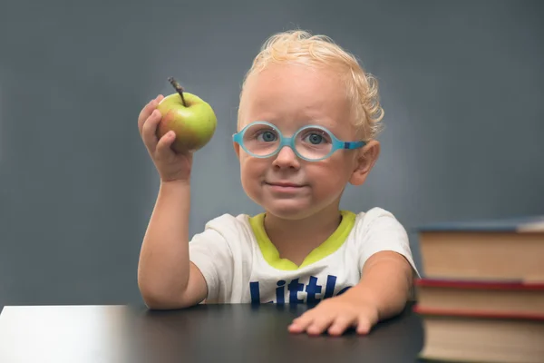 Gözlüklü çocuk kitapları ve elma ile bir masada oturur