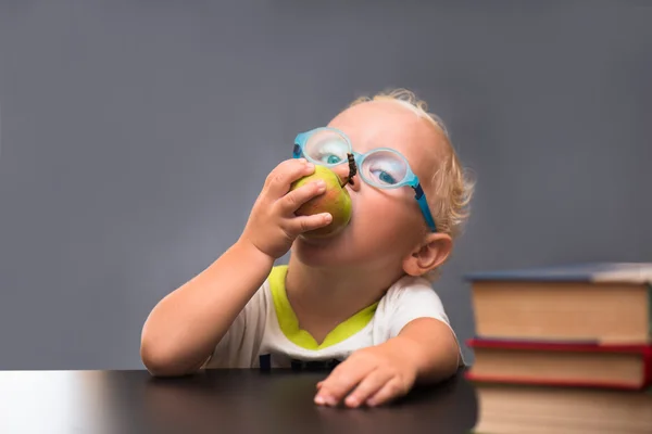 Ребенок в очках сидит за столом с книгами и яблоком — стоковое фото