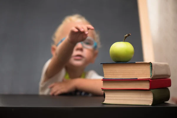 Criança com copos senta-se em uma mesa com livros e maçã — Fotografia de Stock