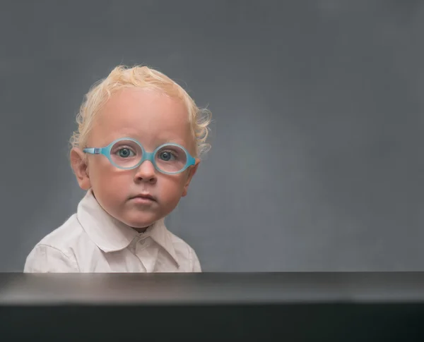 Грустный ребенок в очках сидит за столом — стоковое фото