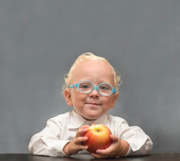 Мальчик с яблоком в очках, сидит за столом — стоковое фото