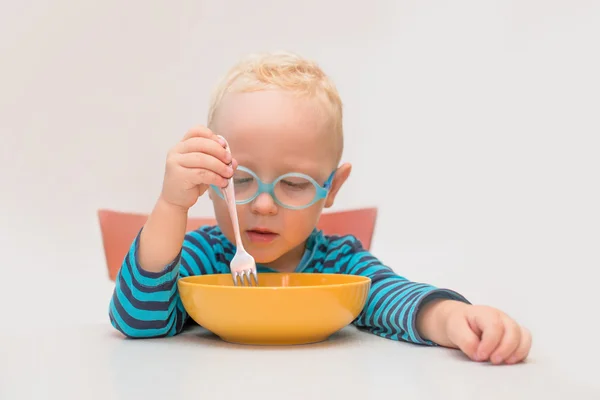 Мальчик в очках сидит за столом перед желтой тарелкой — стоковое фото