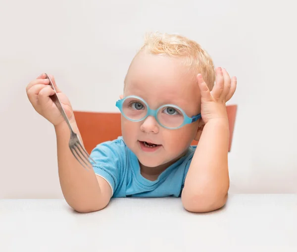 Menino com óculos senta-se em uma mesa na frente de uma placa amarela — Fotografia de Stock