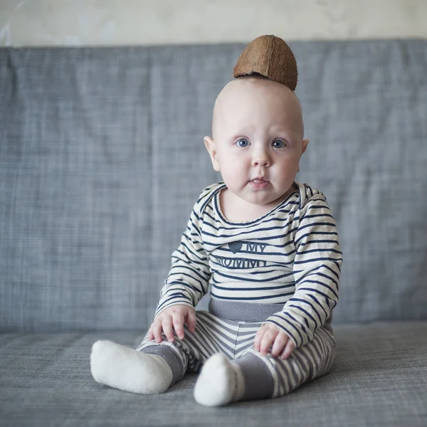 Kleiner Junge sitzt auf der Couch mit einer Kokosnuss auf dem Kopf — Stockfoto