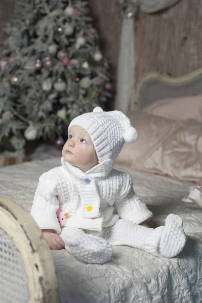 Baby sitting on a bed on the background of Christmas tree — Stock Photo, Image