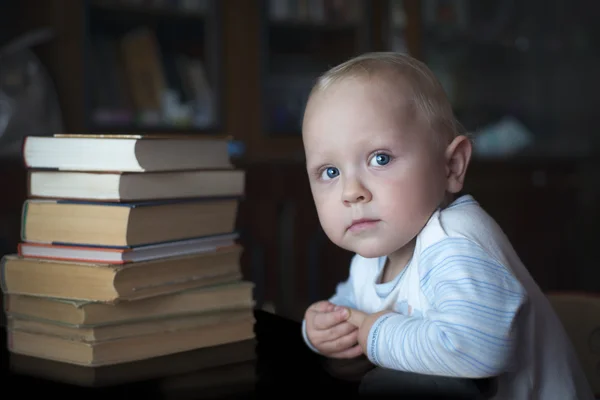 Розумний маленький хлопчик сидить за столом з книгами — стокове фото