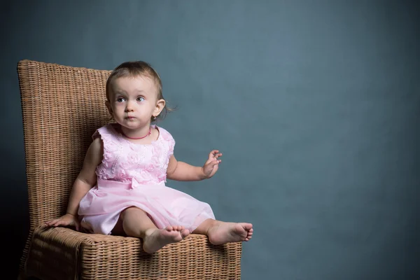 Маленька дівчинка в рожевій сукні сидить на стільці — стокове фото