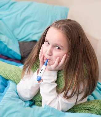 Ağzında bir termometre ile yatakta yatan bir hasta bebek