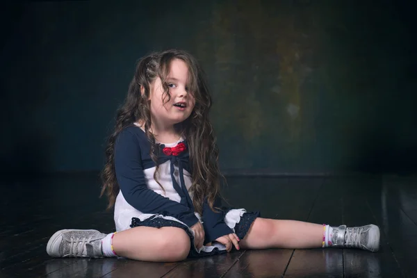 Забавная маленькая девочка с длинными волосами, сидящая на полу — стоковое фото