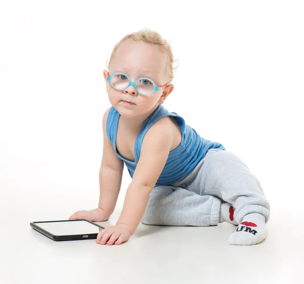 Bir tablet ile katta oturan gözlüklü küçük çocuk