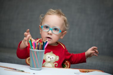 Kağıt ve renkli kalemler ile masa başında oturan bir çocuk