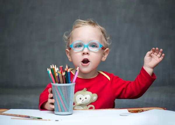 Ребенок сидит за столом с бумагой и цветными карандашами — стоковое фото