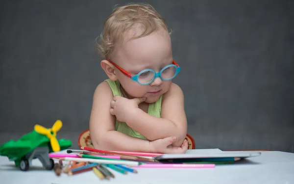 Kağıt ve renkli kalemler ile masa başında oturan bir çocuk