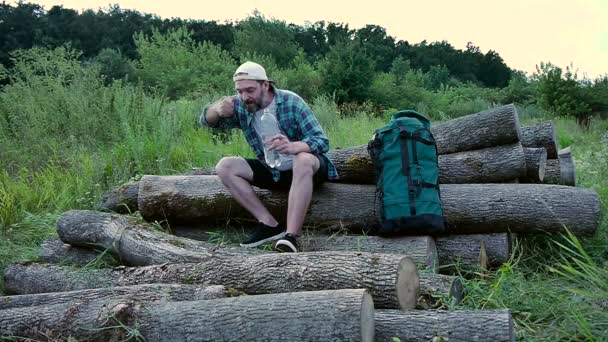 A bearded man with a backpack sitting on logs and washes. — Stock Video