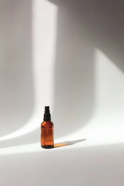 mockup of cosmetic aroma spray in brown bottle on a grey background with shadows. minimalist beauty cosmetic concept