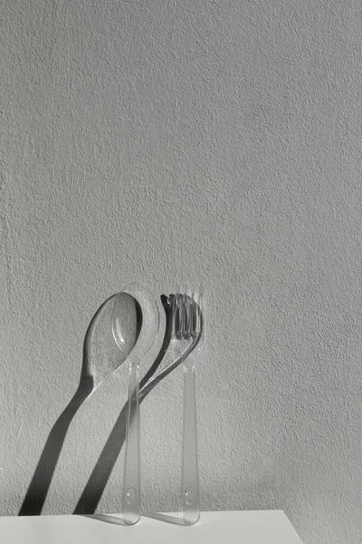transparent  plastic spoon and fork cutlery in the sun with hard shadows. plastic pollution. copy space