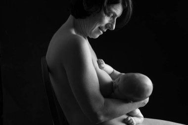 Çocuğunu emziren bir annenin yan görünüşü, siyah arka planda ten tene, siyah beyaz