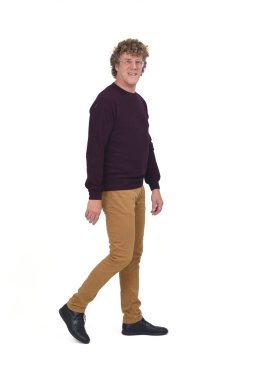 Beyaz arka planda yürüyen kıvırcık saçlı bir adamın yan görüntüsü. Kameraya bakıyor.