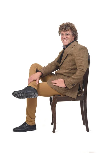 椅子に座ってカメラを見て足を組んで白い背景で笑っている中年男性の側面図です — ストック写真